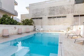 A swimming pool with lounge chairs and a concrete building in the background. - La Gemma del Salento (Racale)