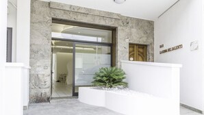 A modern hotel entrance with a marble facade, a glass door, and a small planter with green plants. - La Gemma del Salento (Racale)