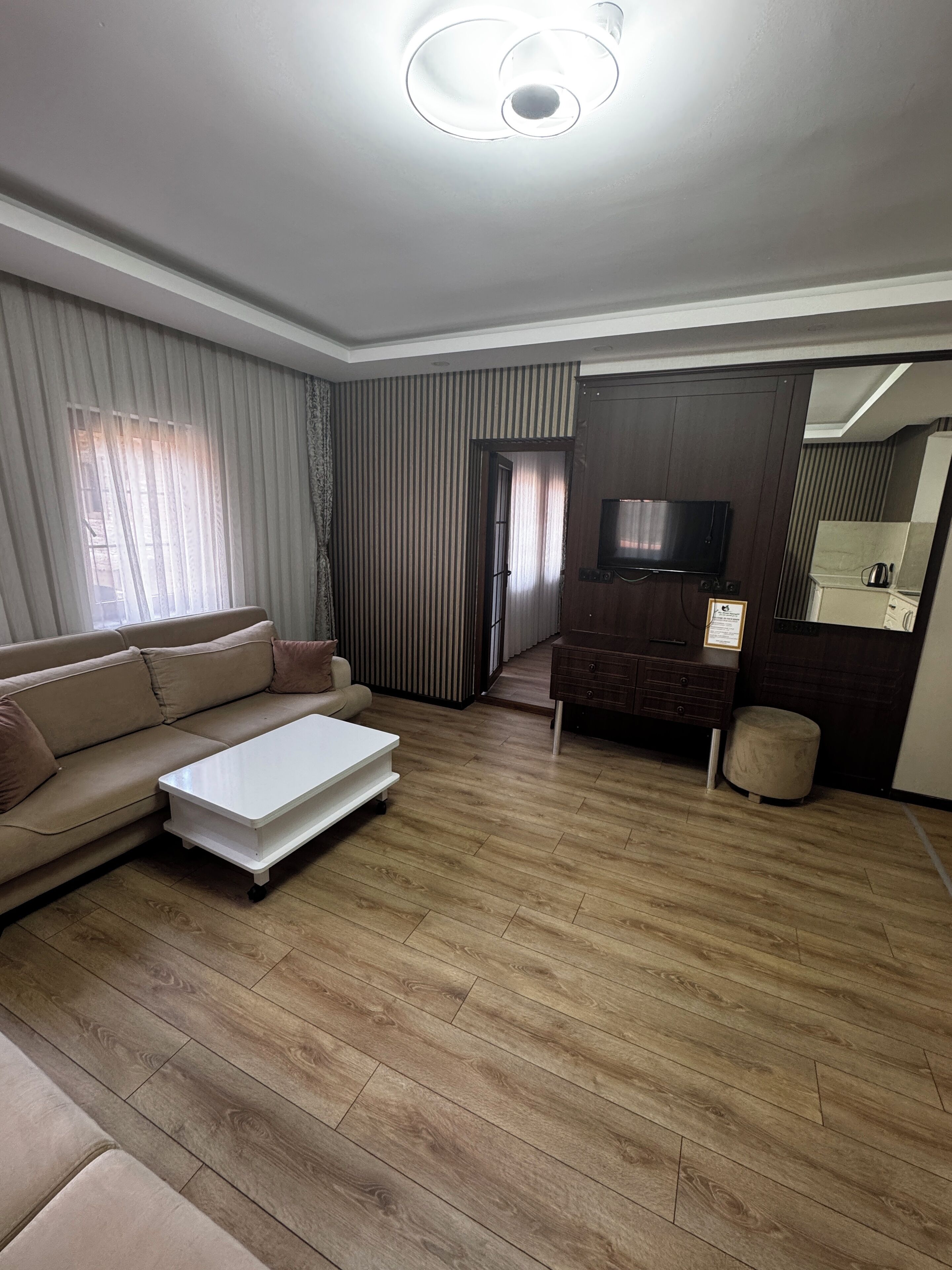 A living room with a sofa, a coffee table, a TV, and a small kitchenette area with a mirror and a cabinet.