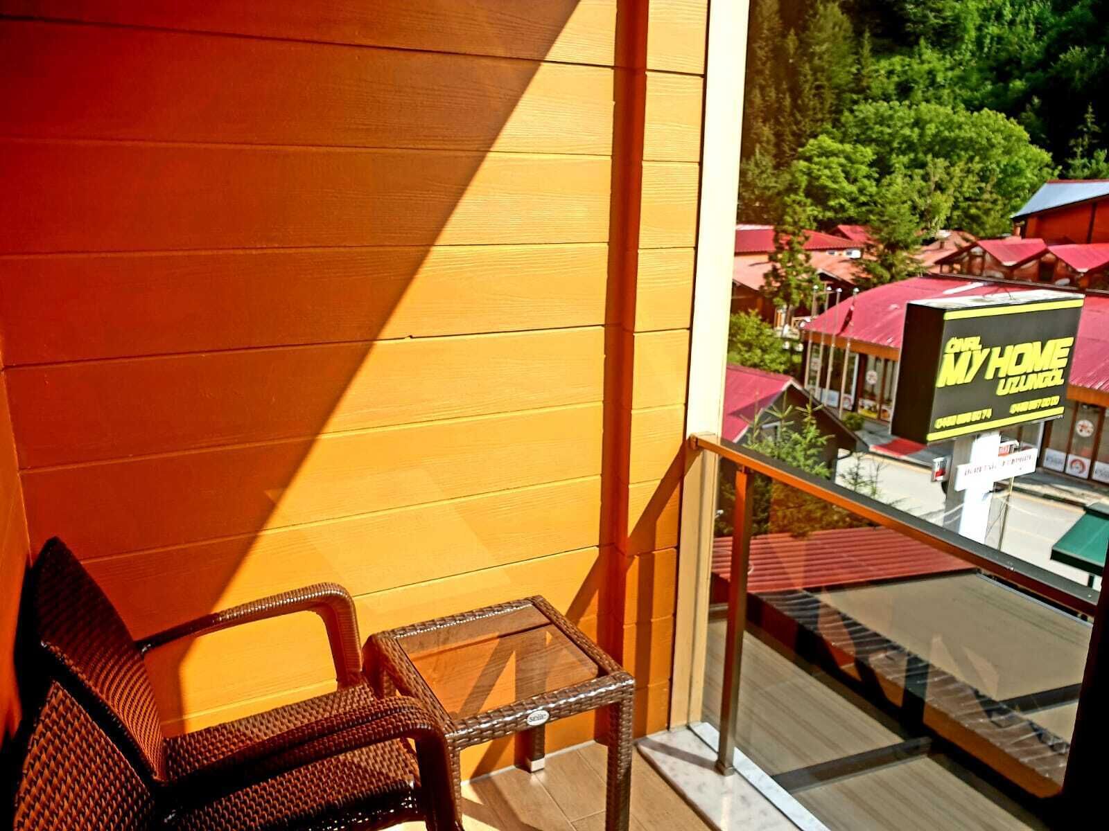 A balcony with wicker furniture, a glass table, and a view of a restaurant with a yellow sign.