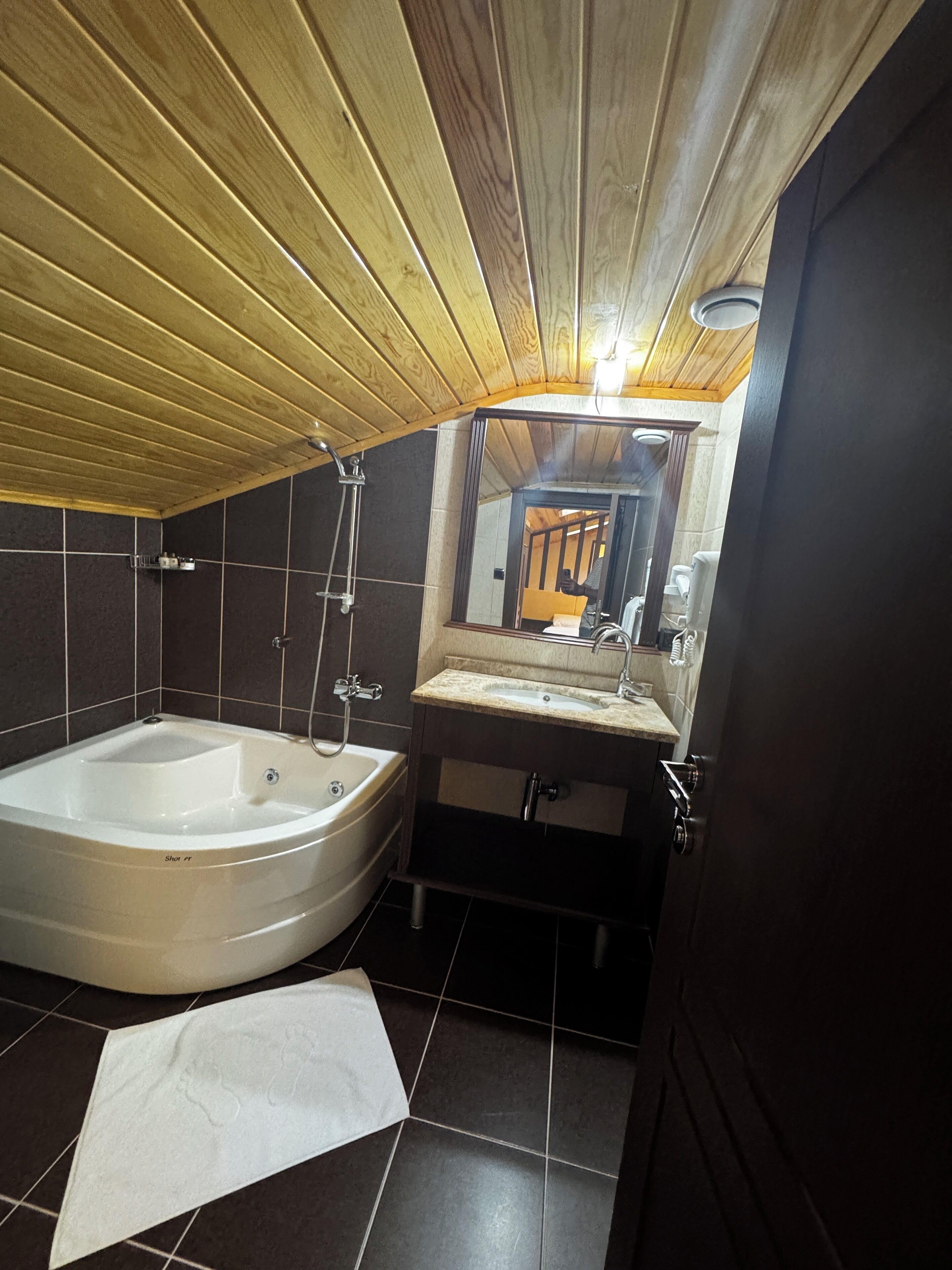 A bathroom with a wooden ceiling, a bathtub, a sink, and a mirror.