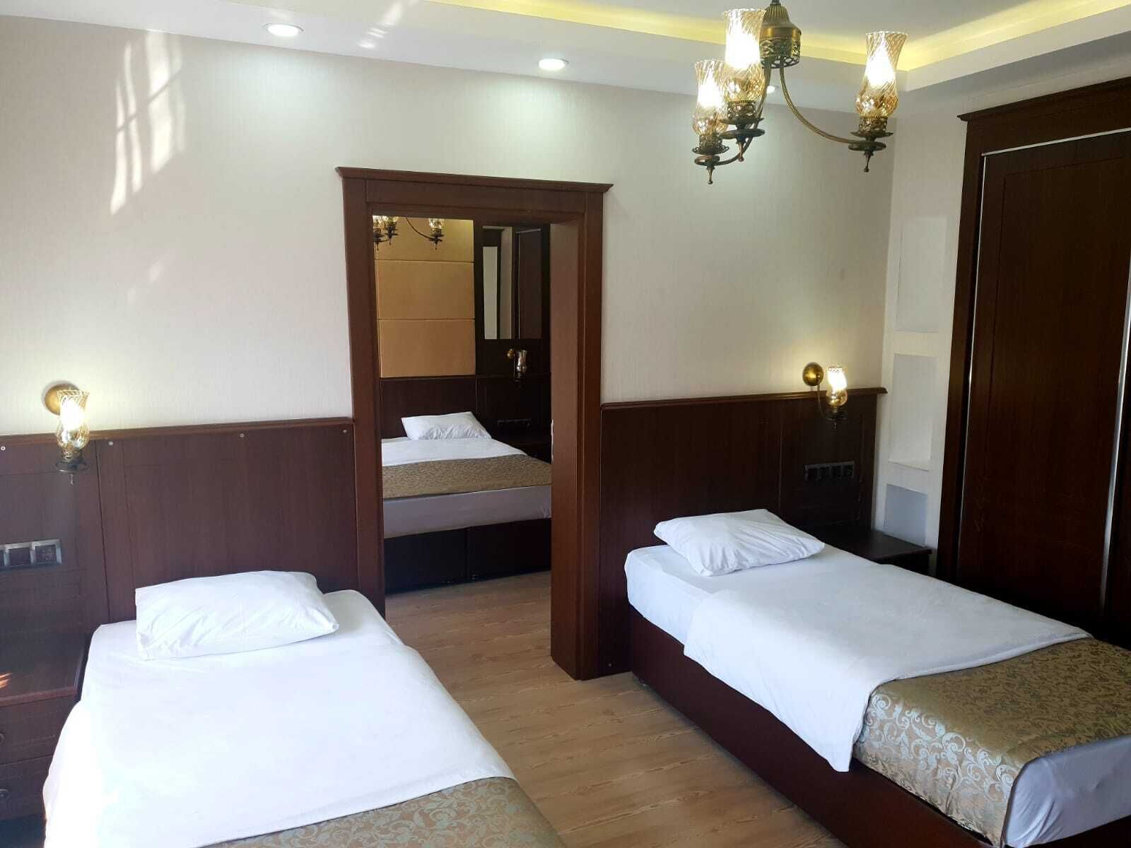 Habitació d'hotel amb dos llits individuals, ambres de fusta, una porta de fusta i un mirall a la paret.
