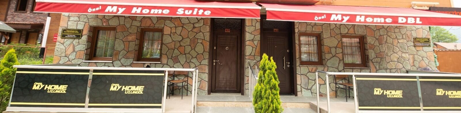 Un hotel llamado "My Home Suite" con fachada de piedra, una puerta de entrada central y mesas al aire libre.
