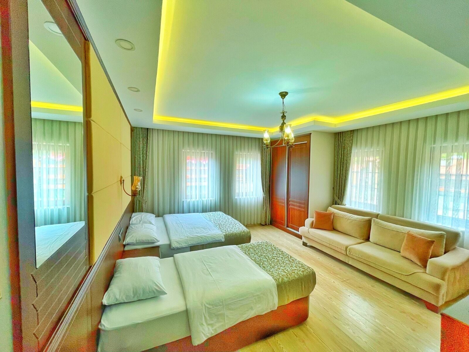 A hotel room with two beds, a sofa, a mirror, and a chandelier.