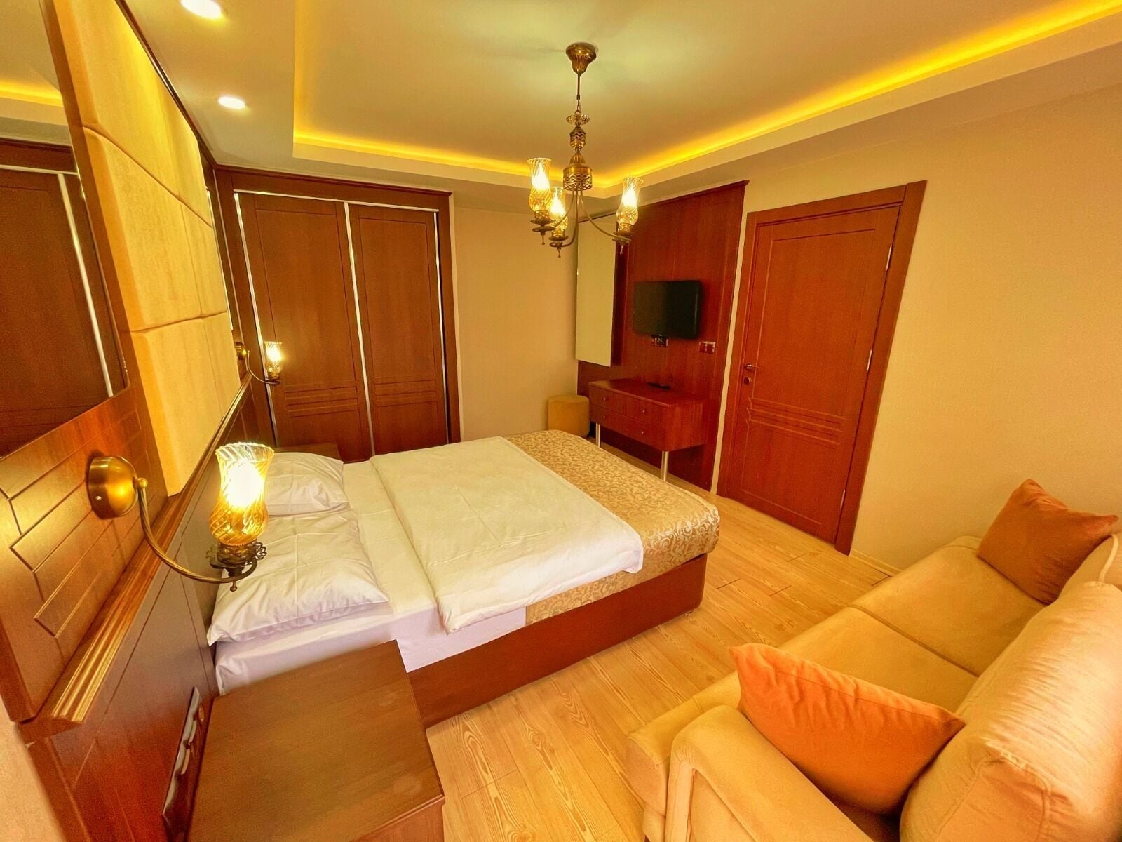 A hotel room with a bed, a sofa, a TV, and wooden wardrobes.