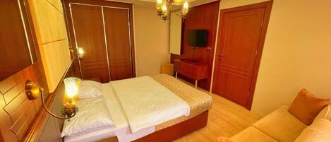 A hotel room with a bed, a sofa, a TV, and wooden wardrobes.