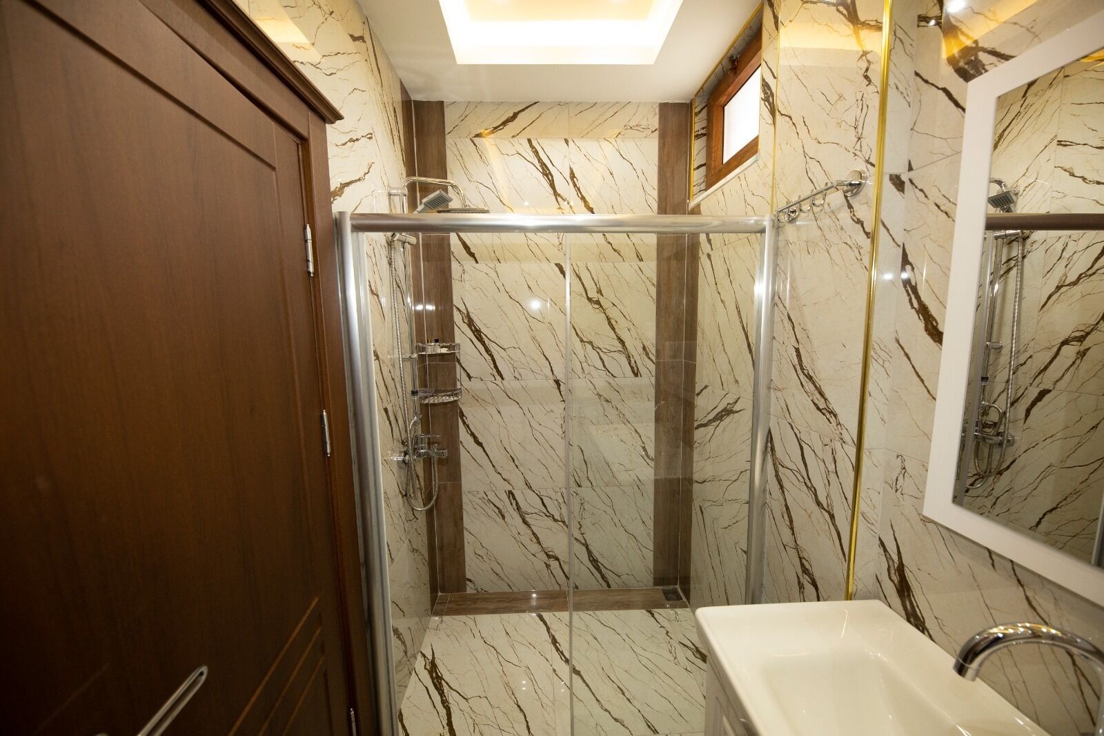 A bathroom with a glass-enclosed shower, marble walls, and a wooden cabinet.