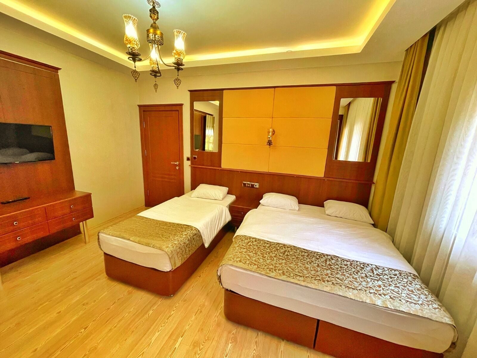 A hotel room with two beds, a TV, a wooden dresser, a chandelier, and a mirror.