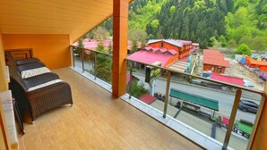 A balcony with wicker furniture, a view of a forested mountain, and a red-roofed building in the background. - My Home Uzungol (Çaykara)