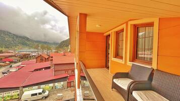 A balcony with a wicker sofa and a view of a town with red-roofed buildings and a lake.