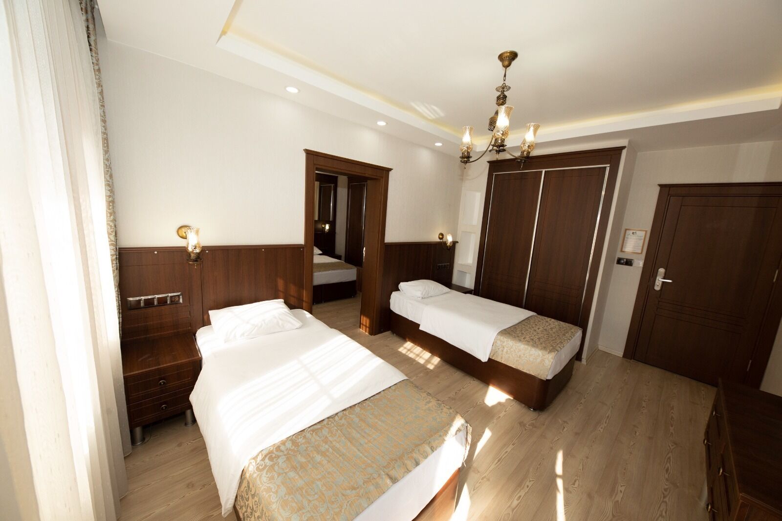 A hotel room with two beds, wooden headboards, a chandelier, and a wardrobe.