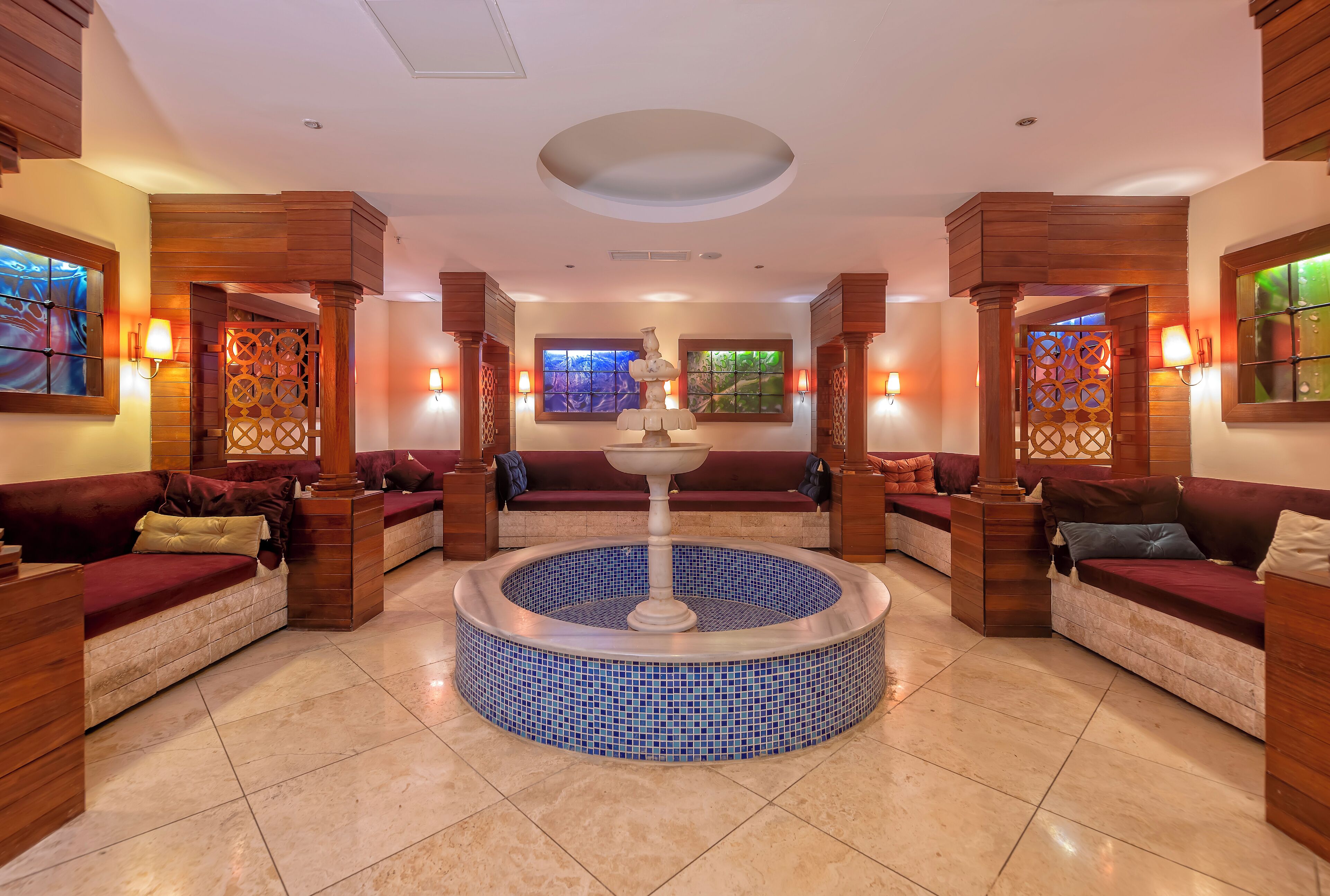 Un espace spa doté d’un grand bain à remous central, de sièges en bois et de panneaux muraux décoratifs.