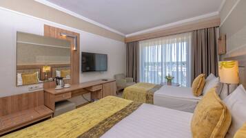 A hotel room with two beds, a desk, a television, and a window with curtains.