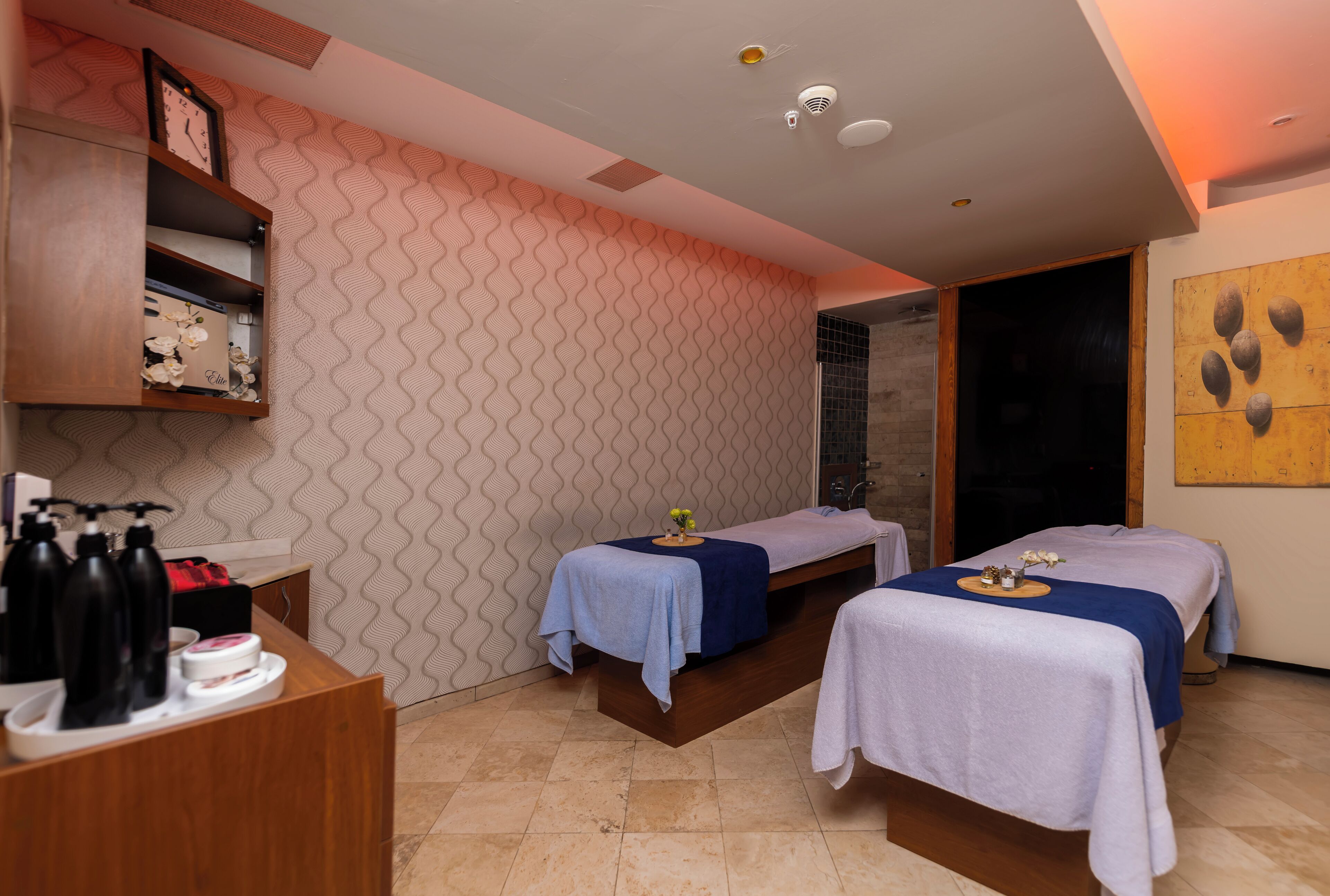 A spa room with two massage tables, a reception desk, and a wall with a wavy pattern.