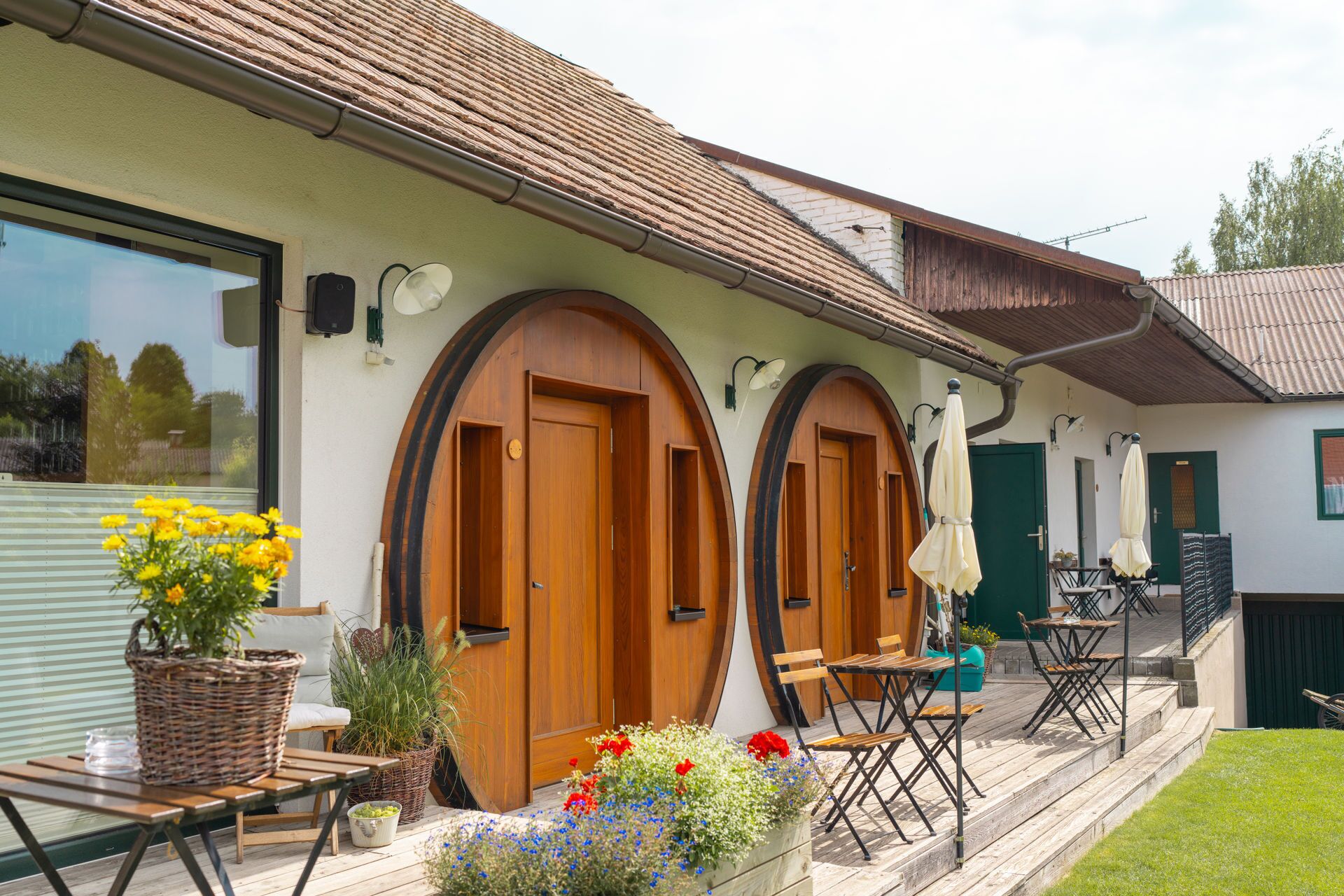 Una casa con dos puertas de madera, un balcón con mobiliario exterior y un jardín lleno de flores.