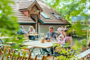 An outdoor dining area with wooden tables and chairs, a building with a sloped roof, and a sign in the background. - Winzerhof Küssler, Weinviertel (Angern an der March)