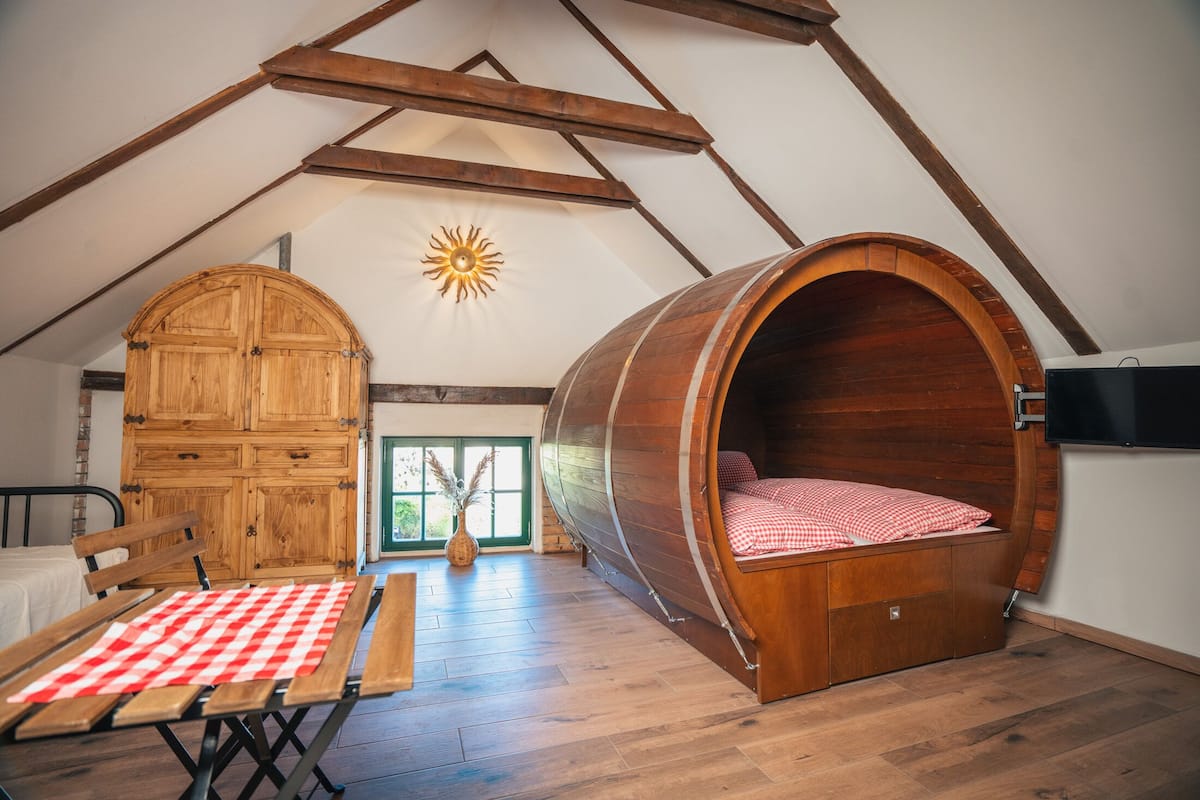 A loft bedroom with a wooden barrel bed, a wooden wardrobe, and a picnic table.