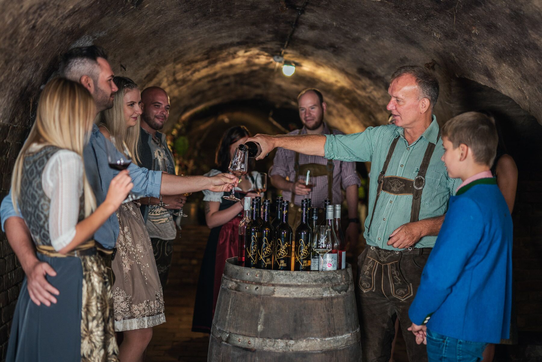A group of people in a dimly lit, tunnel-like space with a wooden barrel filled with bottles.