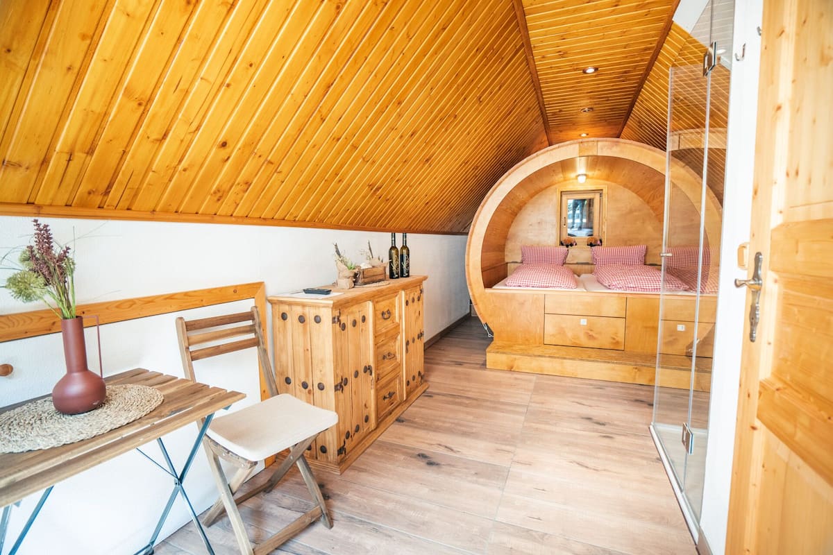 A cozy wooden interior with a round bed, a wooden cabinet, and a small table with a vase.