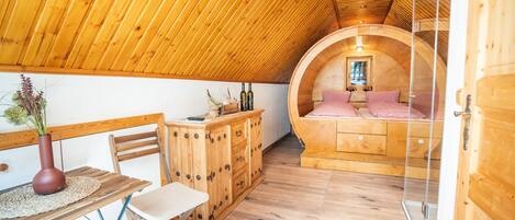 Un interior de madera acogedor, con una cama redonda, un aparador de madera y una mesita con un florero.