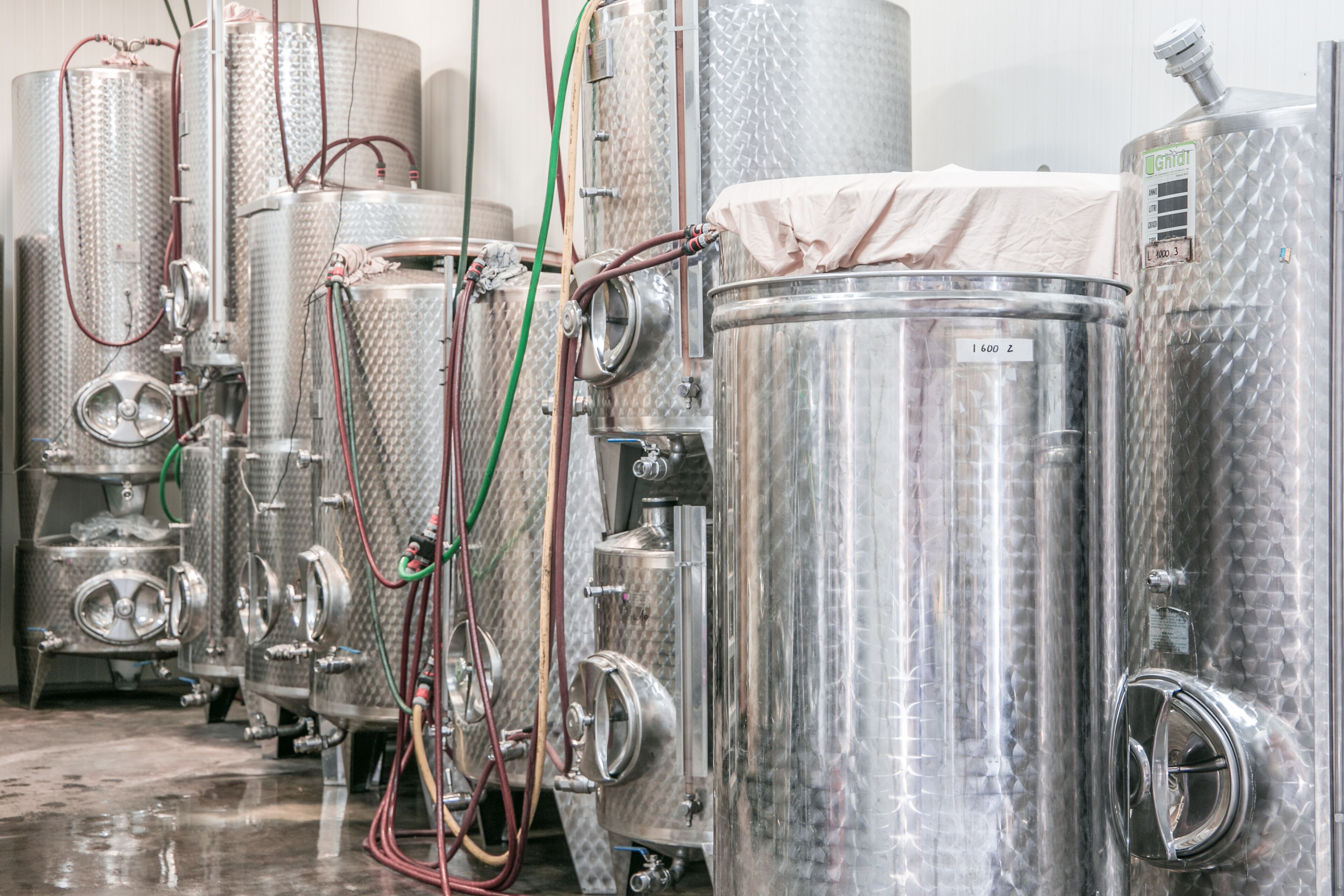 Stainless steel fermentation tanks with hoses and valves, likely used for brewing or fermentation processes.