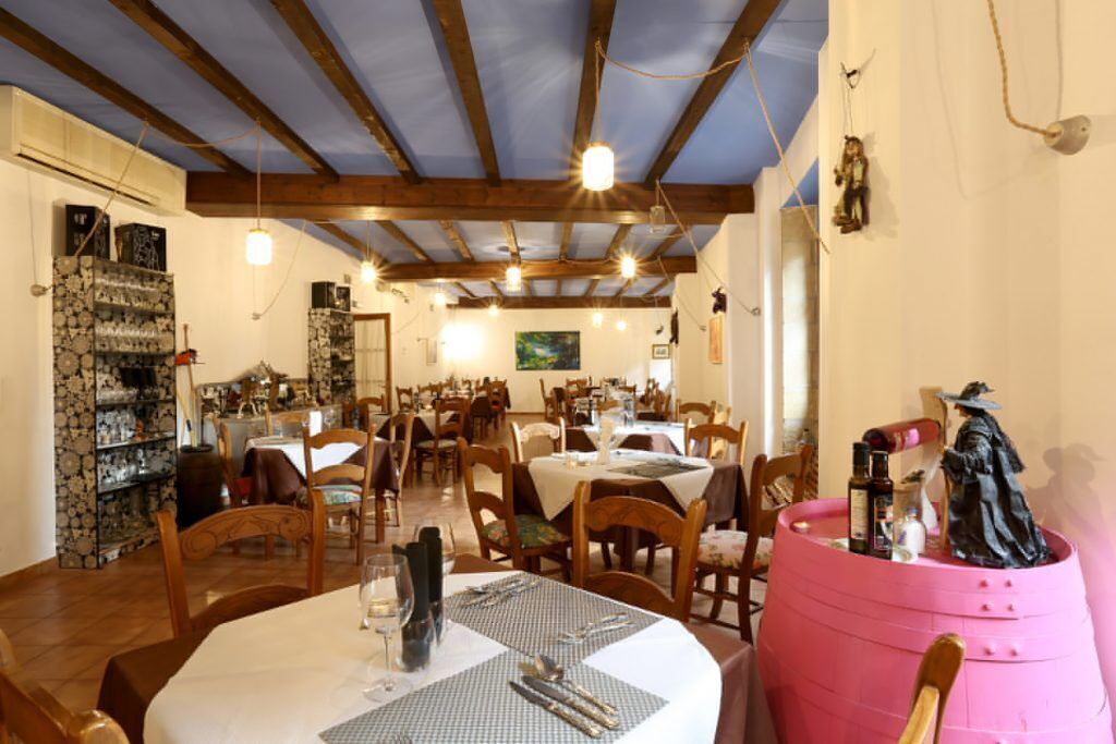 Un comedor con vigas de madera, mesas dispuestas para comer y una estatua sobre un barril.