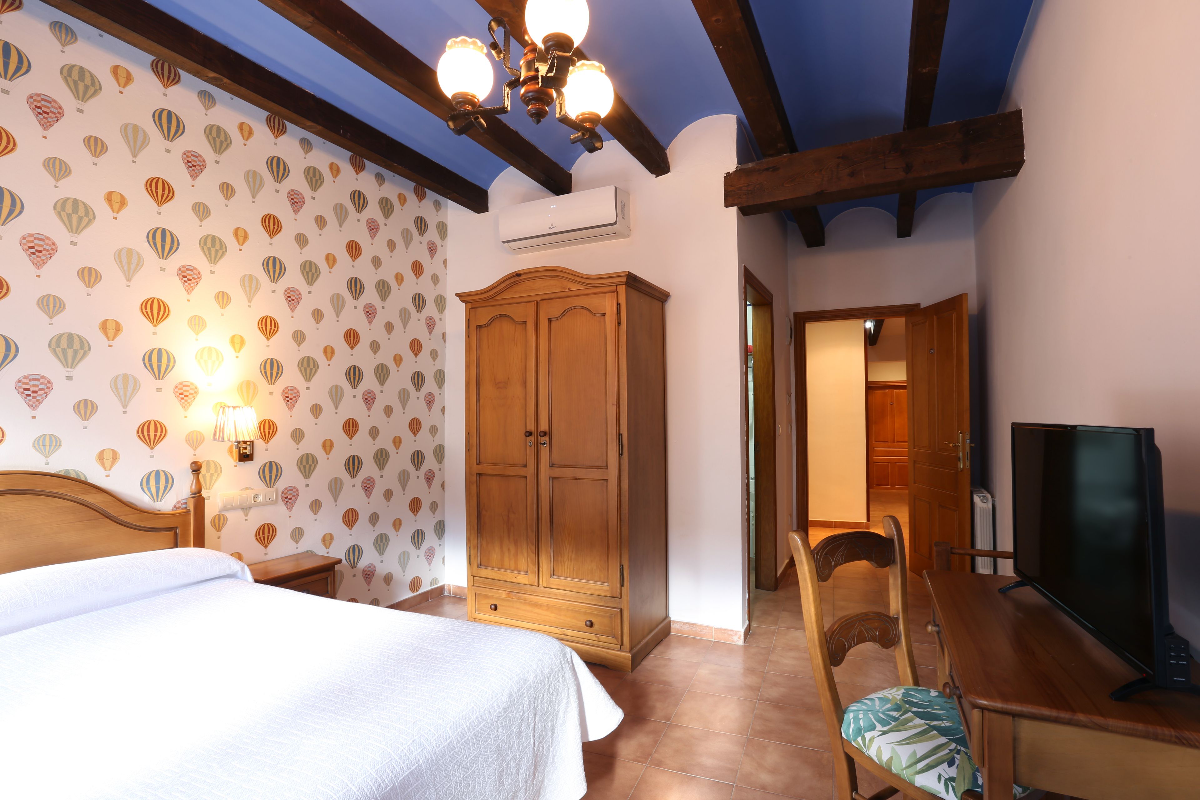 A bedroom with a bed, wooden wardrobe, TV, and a dining table with chairs.