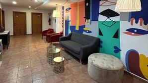 A spacious living area with a sofa, ottoman, and a colorful abstract mural on the wall. - Hospedería de Sádaba (Sadaba)