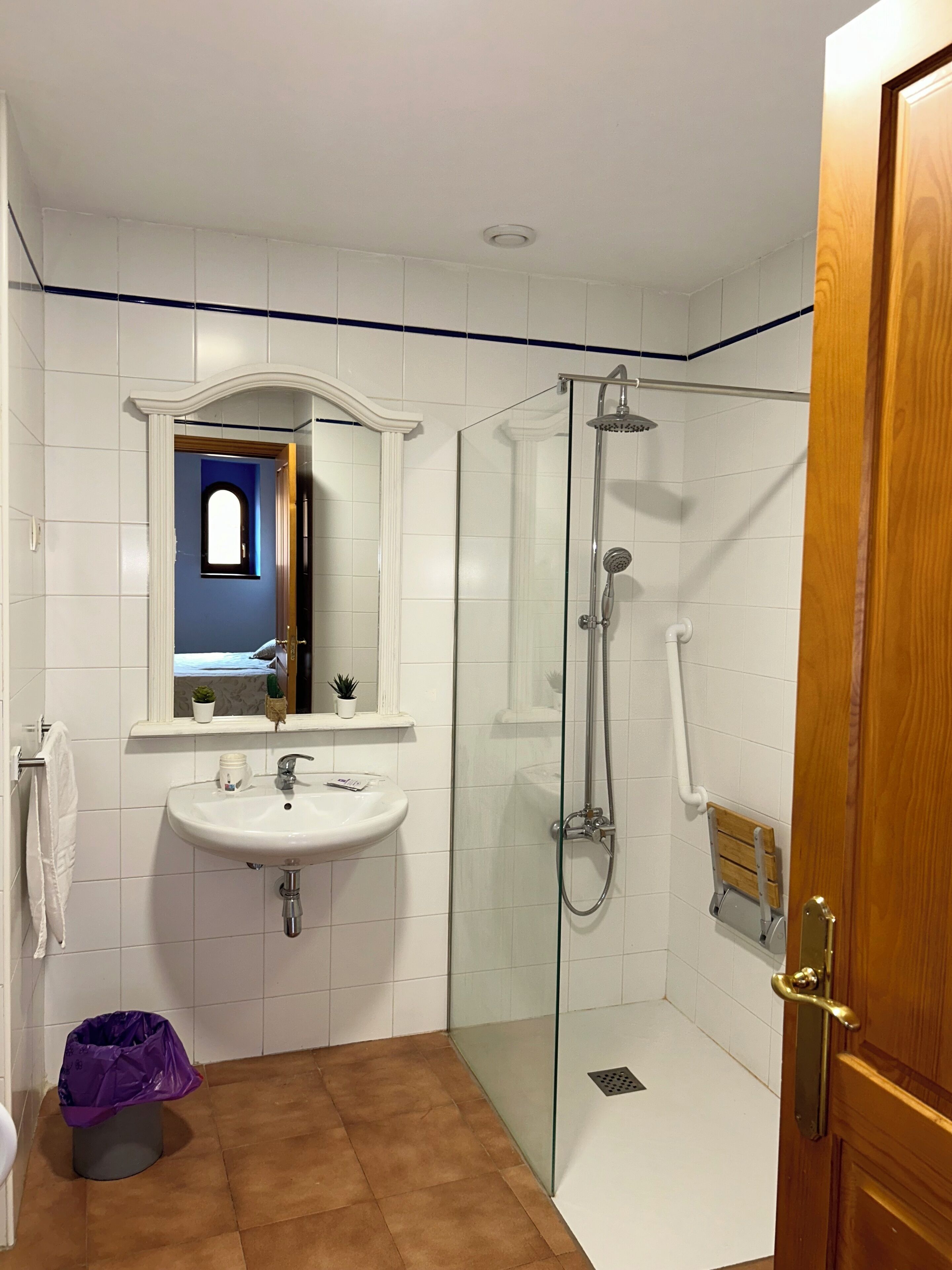 Un baño con un lavamanos blanco, una ducha con cerramiento de vidrio y una puerta de madera.