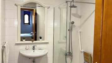 Un baño con un lavamanos blanco, una ducha con cerramiento de vidrio y una puerta de madera.