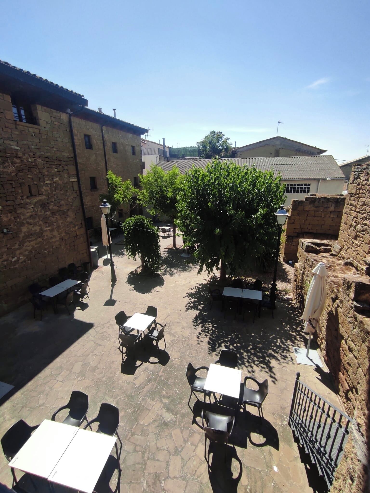 Un cortile esterno con pavimento in pietra, tavoli e sedie disposti per mangiare.