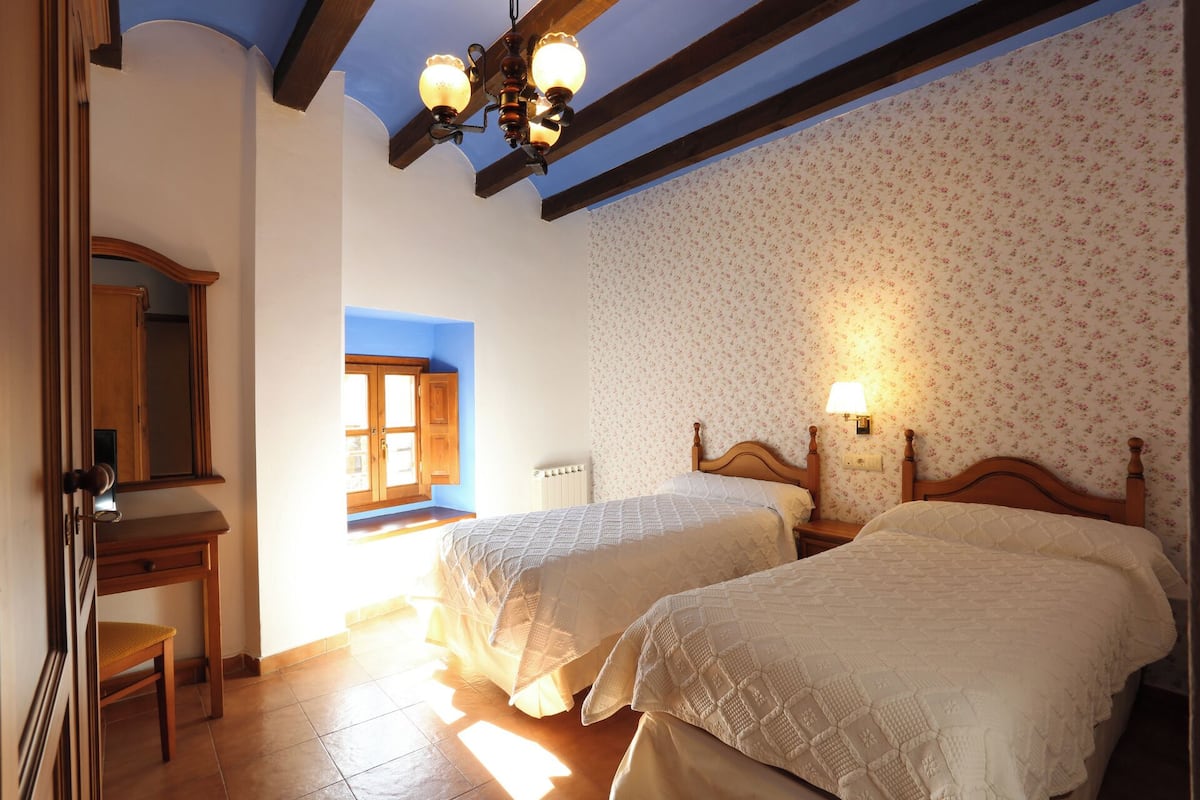 A bedroom with two beds, a wooden dresser, a mirror, and a window with blue trim.