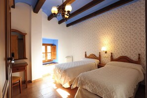 A bedroom with two beds, a wooden dresser, a mirror, and a window with blue trim. - Hospedería de Sádaba (Sadaba)