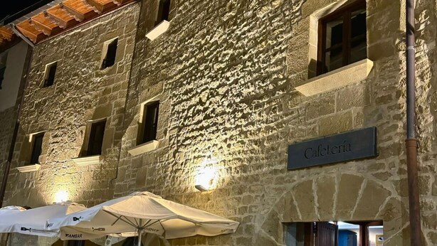 A stone building with a sign reading "Cafetería" and outdoor seating with umbrellas. - Hospedería de Sádaba (Sadaba)