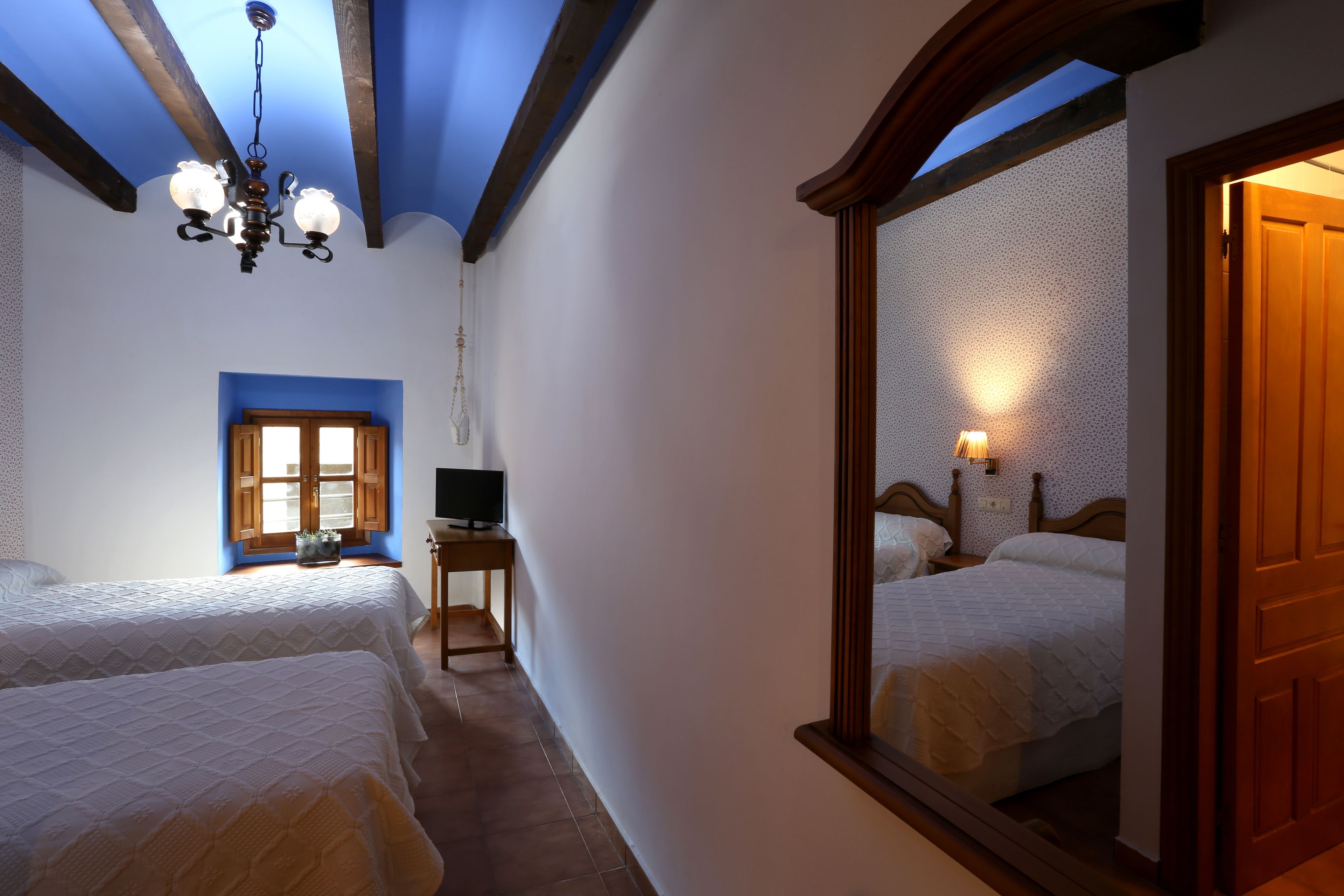A bedroom with two beds, a TV, a small table, and a mirror.
