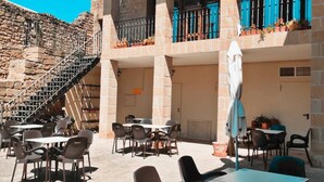 An outdoor café with stone walls, multiple tables and chairs, and a staircase leading to an upper level. - Hospedería de Sádaba (Sadaba)