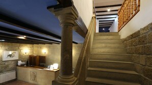 A stone staircase with a wooden handrail leading to a landing. There is a reception desk with a counter and a coat rack. - Hospedería de Sádaba (Sadaba)