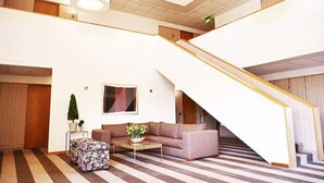 Eine geräumige Lobby mit Treppe, einer Couch, einem Couchtisch und einem Blumentopf.