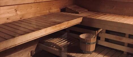 A wooden sauna with benches and a bucket on the floor.