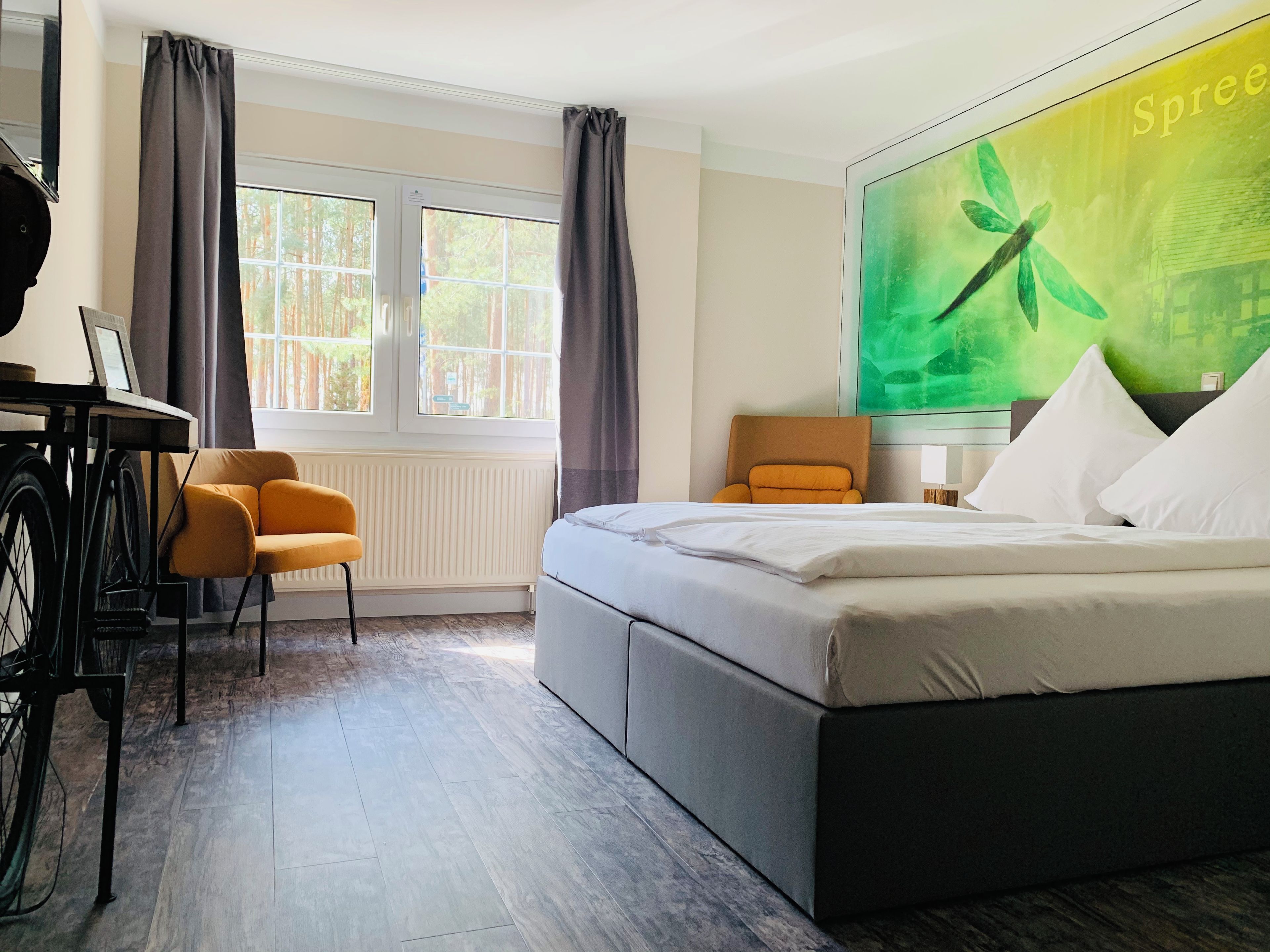 Una habitación de hotel con cama, escritorio, silla, ventana y un cuadro grande en la pared.