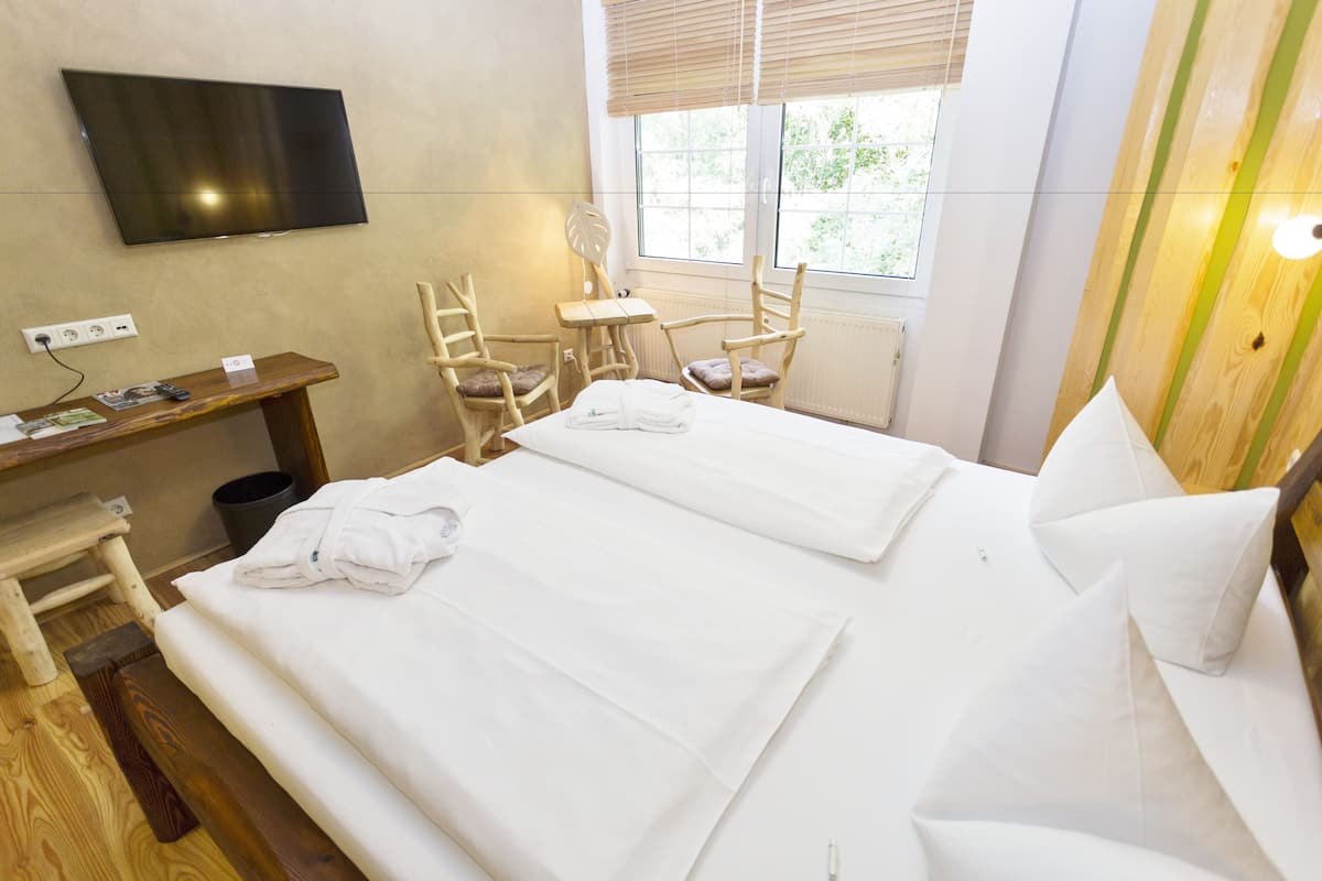 Une chambre d’hôtel avec deux lits, un téléviseur fixé au mur, un bureau avec une chaise et une fenêtre avec des stores.