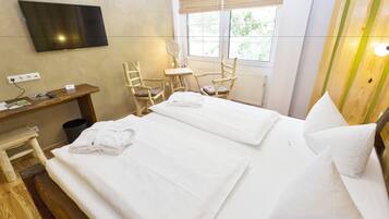 Hotellihuone, jossa on kaksi sänkyä, seinälle asennettu televisio, työpöytä tuolilla ja ikkuna, jossa on sälekaihtimet.