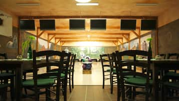 A restaurant with wooden beams, green cushioned chairs, and a bowling lane in the center.
