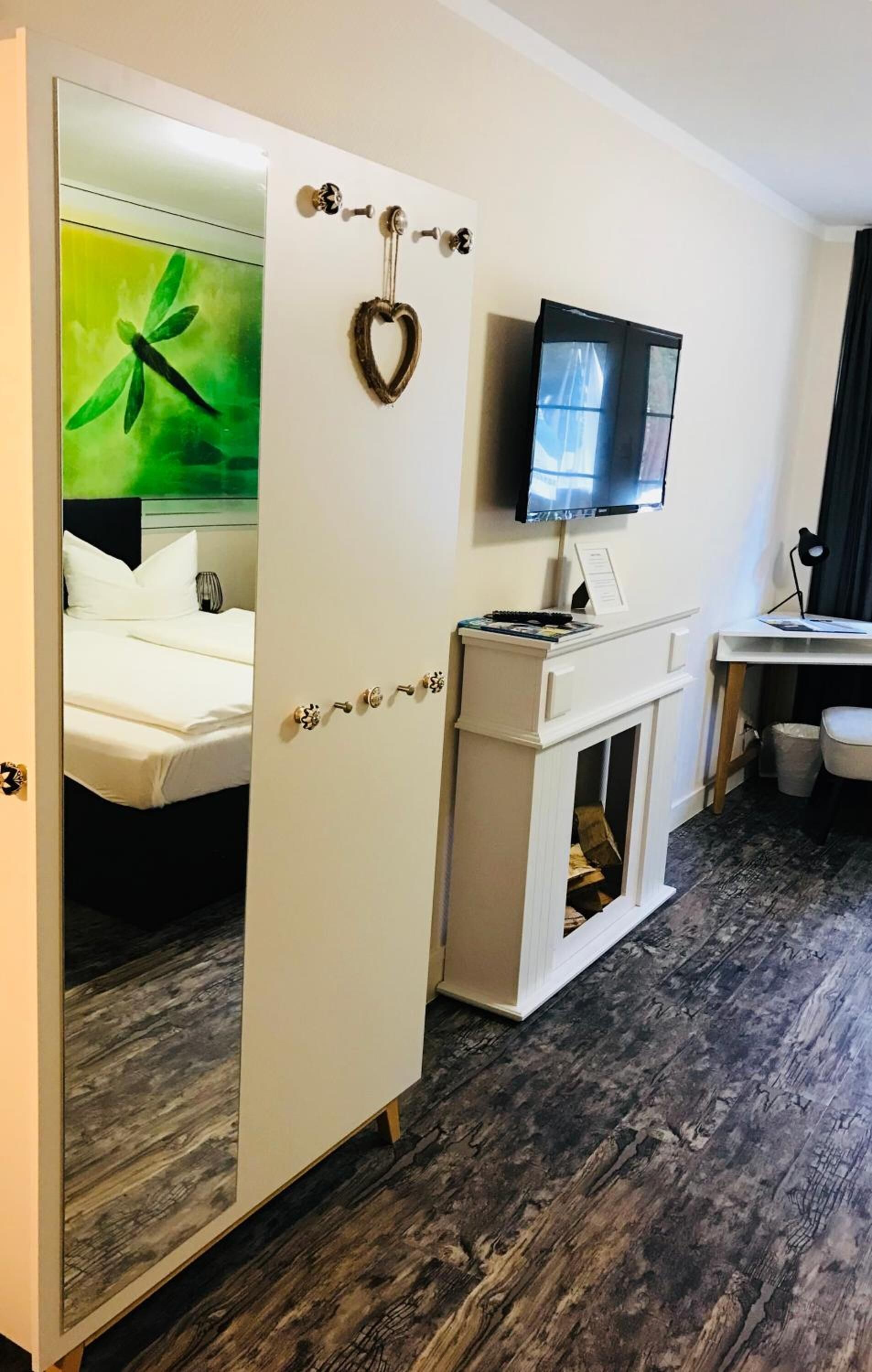 Ein Hotelzimmer mit Bett, Fernseher, Kamin und Spiegel mit einem Gemälde eines grünen Blattes.