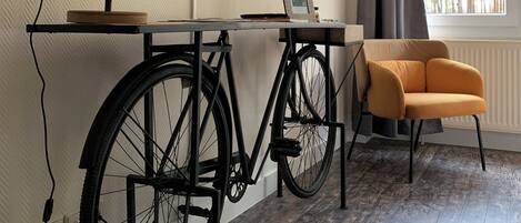 A room with a mounted TV, a bicycle, a chair, and a window with curtains.
