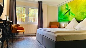 A hotel room with a bed, a desk with a chair, a window with curtains, and a large green painting on the wall. - Spree-Waldhotel Cottbus (Cottbus)