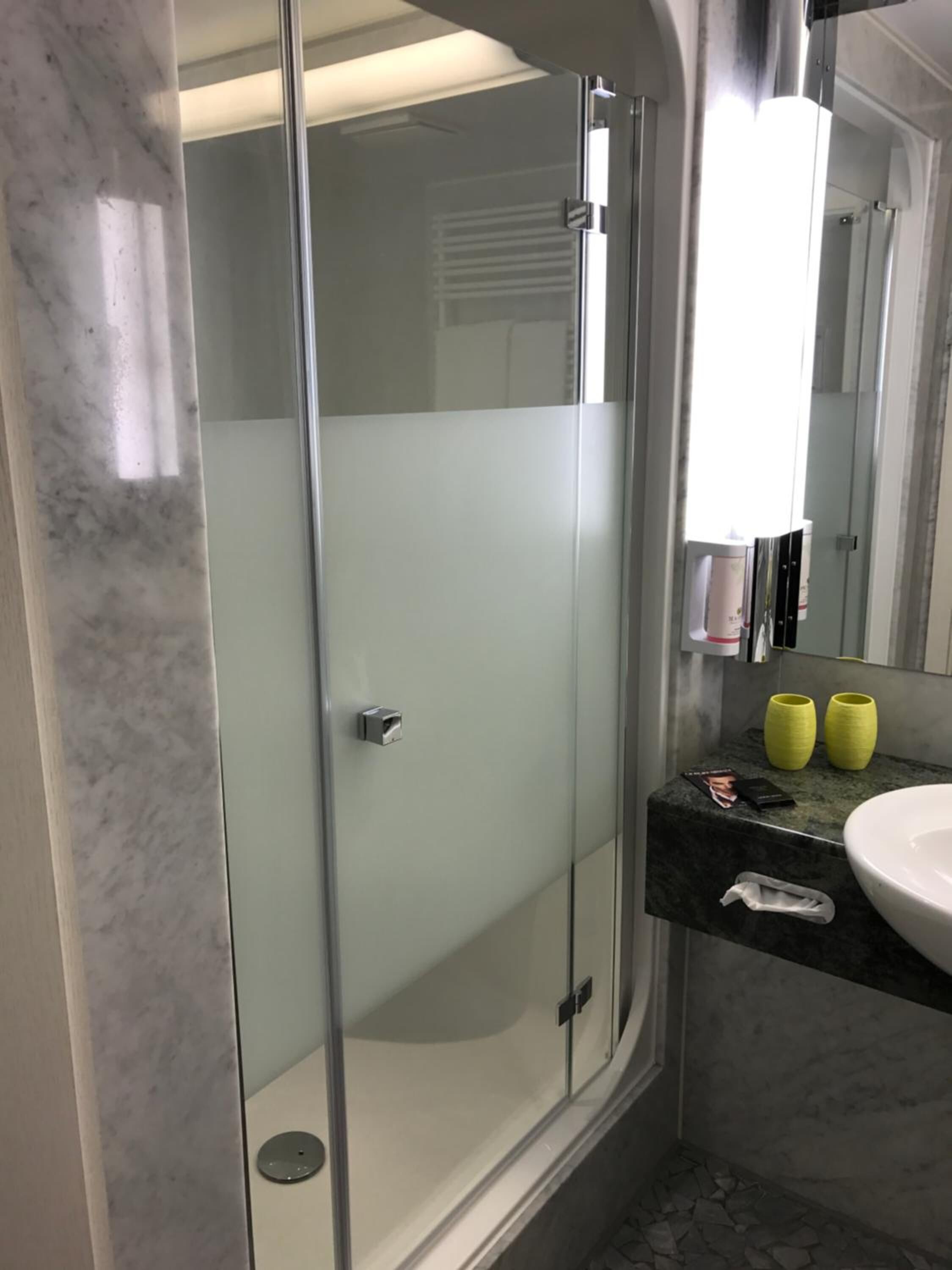 Ein modernes Badezimmer mit einer gläsernen Duschkabine, einem мраморному Waschbecken und einem Spiegel.