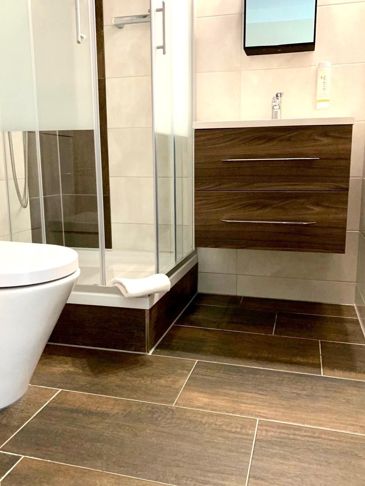 Une salle de bain avec une douche à parois de verre, des toilettes blanches et un meuble-lavabo en bois doté de tiroirs.