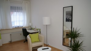 Un salon moderne avec un canapé, une petite table blanche, une lampe sur pied, une plante en pot et un grand miroir accroché au mur.