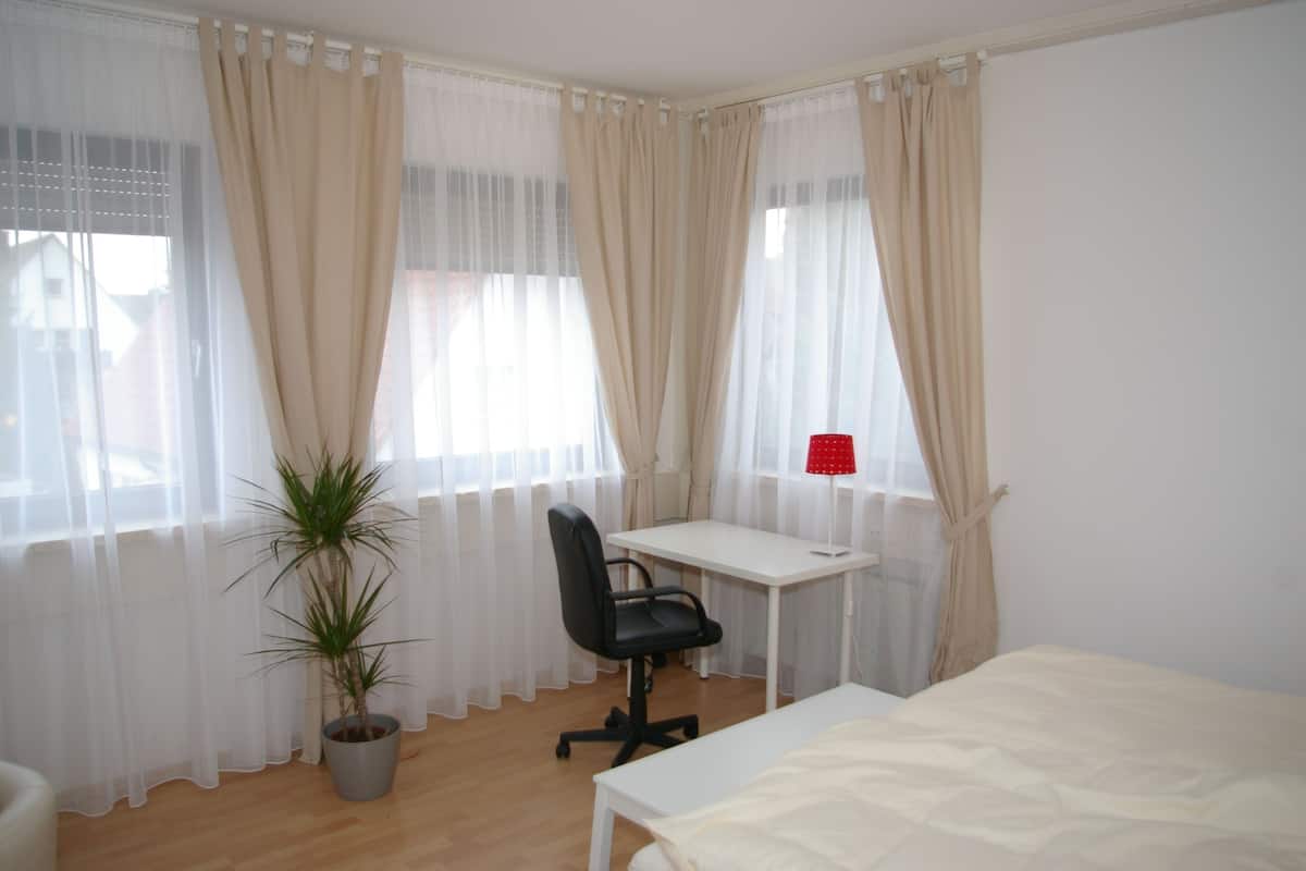 A bedroom with a bed, a desk, a chair, and a potted plant.